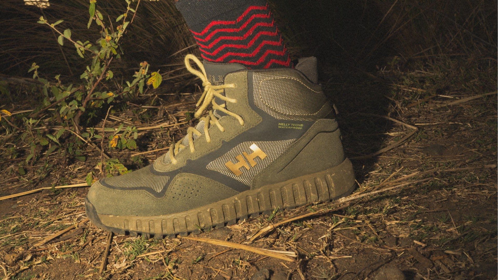 Close-up of a Helly Hansen hiking boot and red patterned sock on dry grass at night