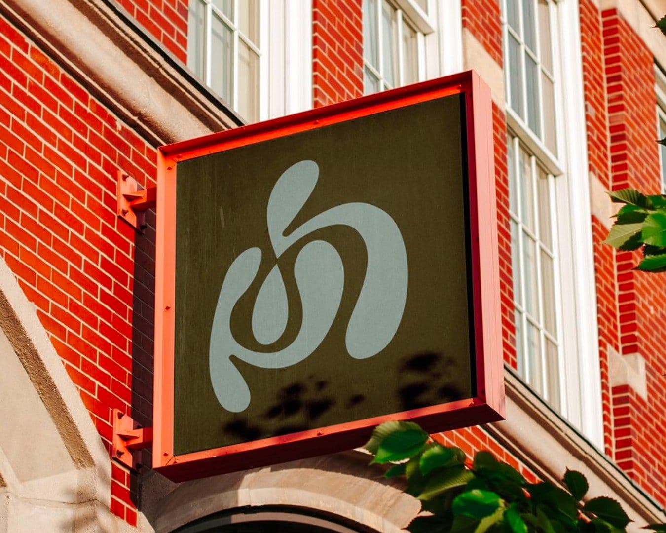 An olive House of Pilates sign with the mark in sage, mounted on a red-brick facade