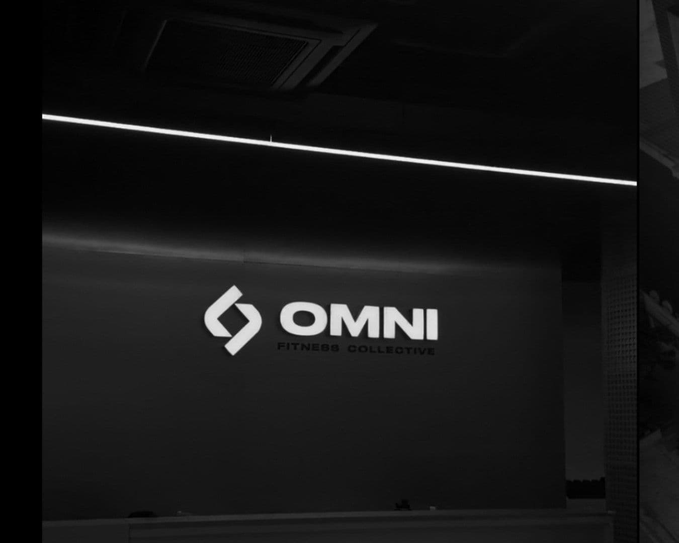The OMNI Fitness Collective logo lit on a dark gym wall