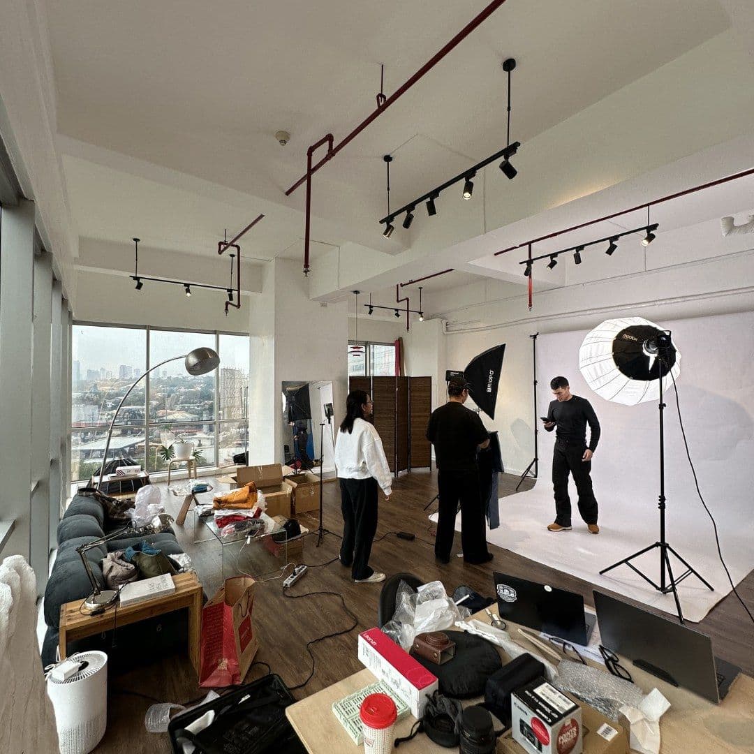 The Open Concept photo studio mid-shoot: lighting rigs, a white backdrop and the crew at work, with the city skyline through the windows