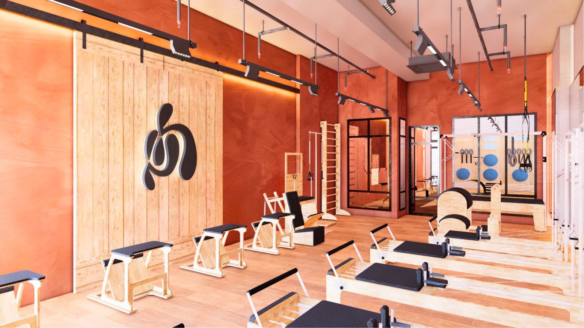 A House of Pilates studio interior with reformers, terracotta walls and the brand mark on a timber wall