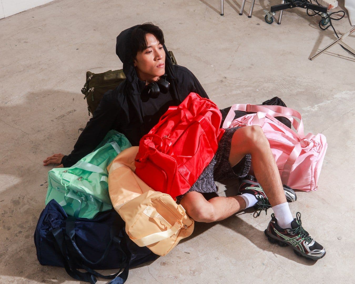 A man lounges on a concrete floor on a pile of colourful 815 duffel bags