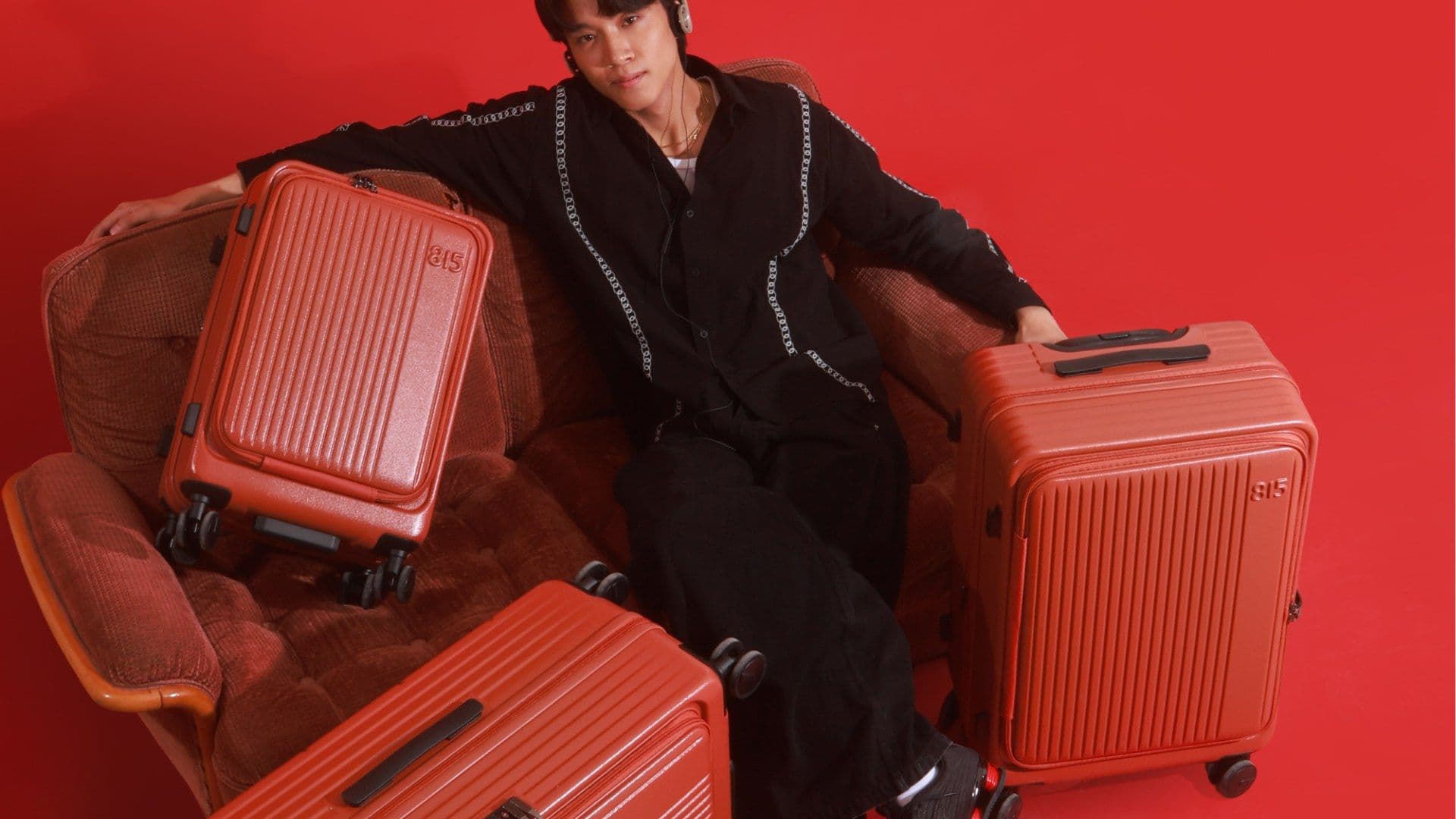 A man reclines on a sofa surrounded by red 815 suitcases against a red wall