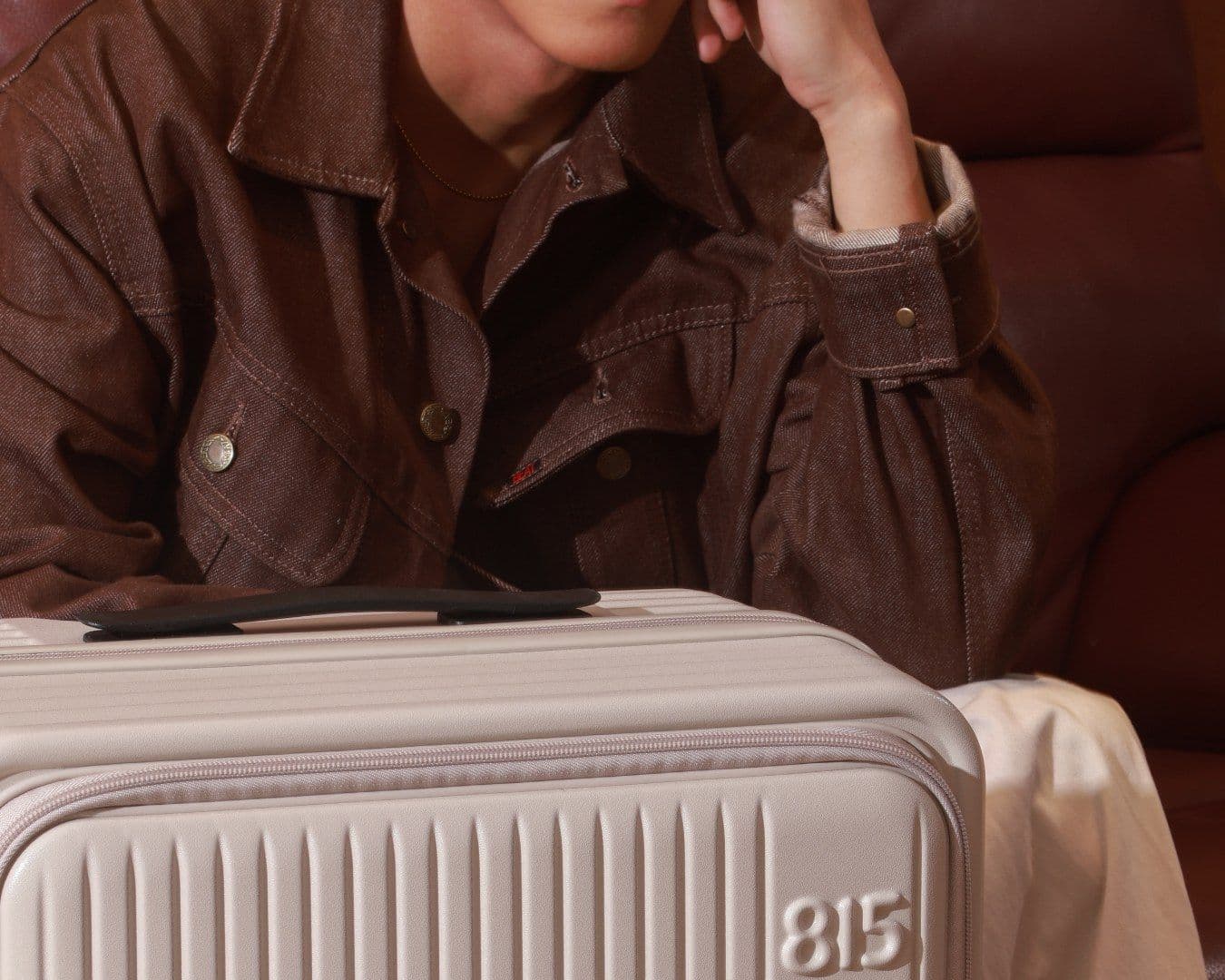 Detail of the embossed 815 logo on a cream suitcase, with a man in a brown jacket behind it